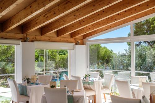 a dining room with white tables and chairs and windows at Hotel Cala Dor - Adults Only in Cala d´Or