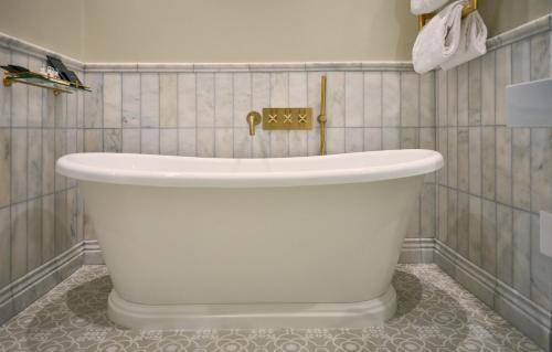 a white tub in a bathroom with a tiled wall at The Tophams Hotel in London