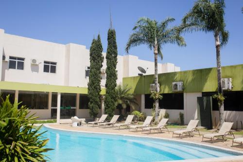 uma piscina com cadeiras e palmeiras em frente a um edifício em Hotel Sol Nascente em Arapiraca