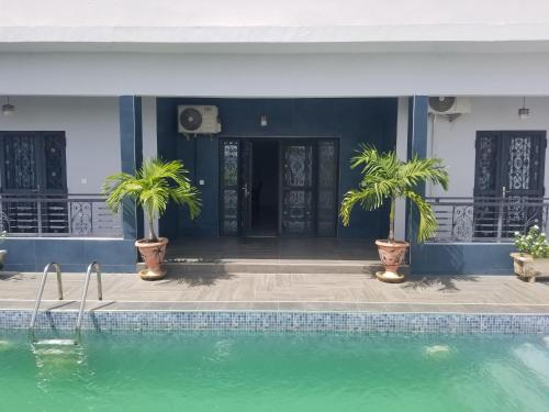 a swimming pool with two palm trees in front of a house at Villa Ndiaye in Ngaparou