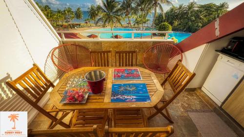 a table and chairs on a balcony with a pool at Ti Kaz Funky Host -T3 vue mer prémium 3 étoiles - Village vacances Sainte Anne Guadeloupe in Sainte-Anne