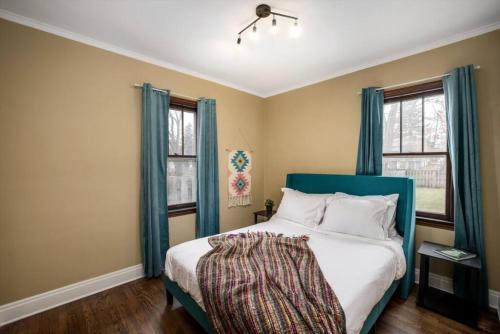 a bedroom with a bed with a blue headboard and two windows at 10 Mins To The Big House and Sleeps Up To 10 Guests in Ann Arbor