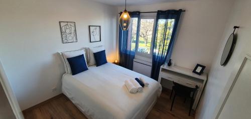 um quarto com uma cama branca com almofadas azuis e uma janela em Maison tout confort aux portes de la ville em La Couronne