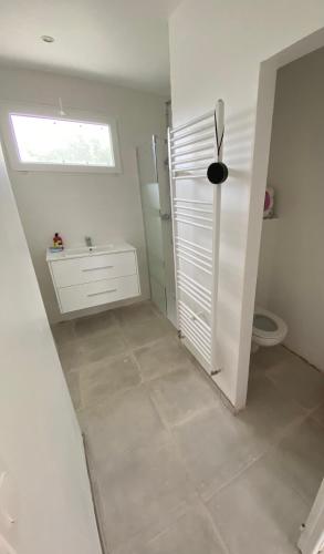 une salle de bain blanche avec toilettes et fenêtre dans l'établissement La maison bleue vacance et jardin, la mer à 550 m, à Blainville-sur-Mer
