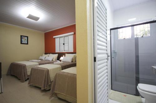 a room with two beds and a bathroom with a toilet at Pousada Recanto Solar dos Pássaros in Olímpia