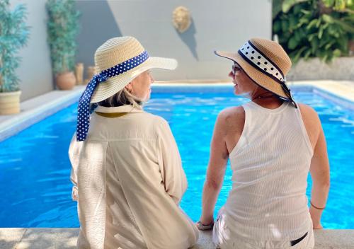 dwie kobiety w kapeluszach siedzące obok basenu w obiekcie Casa Palacio Ánima w mieście Jerez de la Frontera