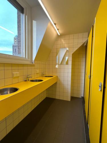 a yellow bathroom with two sinks and a window at Hostel & Bar De Basis in Zwolle