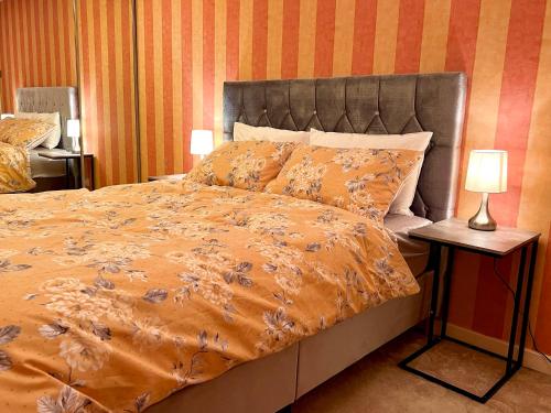 een bed met een oranje dekbed en 2 lampen bij Cheerful 2 Bedroom Home with Off-road parking in Deysbrook