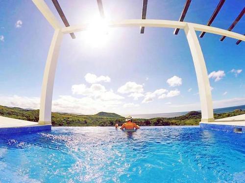 a person in a swimming pool with the sun in the sky at Surf Ranch Resort - Popoyo in Popoyo