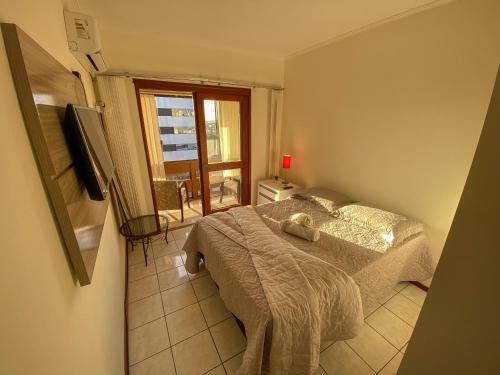 a bedroom with a bed and a window and a television at Apartamento de frente com sacada no centro de Capão da Canoa in Capão da Canoa