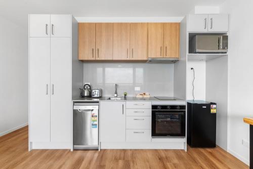 a kitchen with white cabinets and a black refrigerator at Manukau Studio Apartments in Auckland