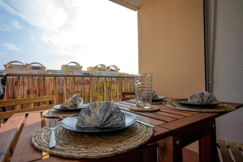 une table en bois avec des assiettes et des verres sur un balcon dans l'établissement Logis des Goélands YourHostHelper, à Gruissan