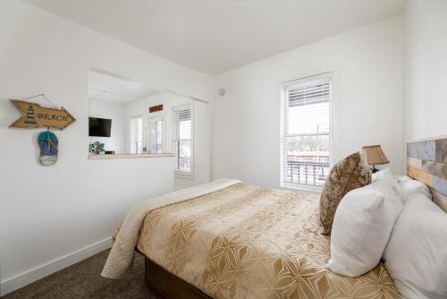 a white bedroom with a bed and two windows at The City Roost at Timberline Flats with Balcony in Traverse City