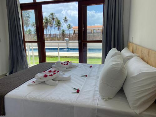 a bed with white pillows and red flowers on it at Pousada Canouan in Japaratinga