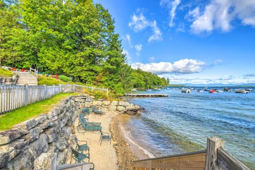 a beach with chairs and a retaining wall next to the water at Gilford Townhome with Lakefront Beach and Pool Access! in Gilford