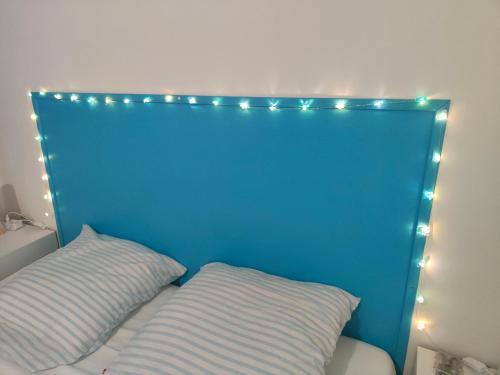 une tête de lit bleue avec des lumières au-dessus de deux oreillers dans l'établissement Bienvenue à la plage !, à Argelès-sur-Mer