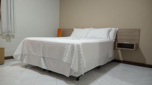 a bedroom with a bed with white sheets and pillows at Pousada Colonial in Macaé