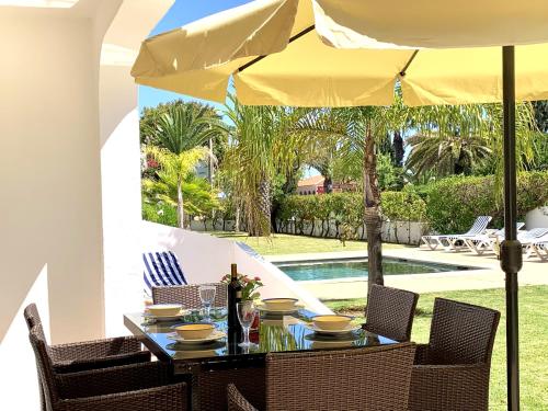 a table with chairs and an umbrella on a patio at 3 bedrooms house at Carvoeiro 650 m away from the beach with shared pool furnished garden and wifi in Carvoeiro