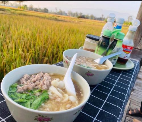 una mesa con dos tazones de sopa y un campo en hueankwankao เฮือนขวัญข้าว, 