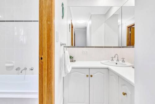 ein weißes Badezimmer mit einem Waschbecken und einem Spiegel in der Unterkunft Laidback Seaford Family Retreat 200m from Beach in Seaford