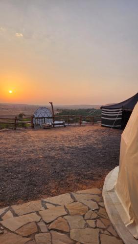 a sunset over a field with a tent and a fence at Bidiyah Domes in Bidiyah
