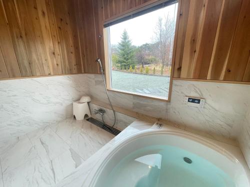 a bathroom with a bath tub with a window at 薪ストーブサウナ付き250平米大型豪華フィンランドログ in Miyota