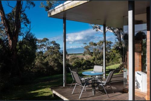 a table and chairs on a porch with a view of the ocean at Mt Singapore Villas - Villa 1 in Yanakie