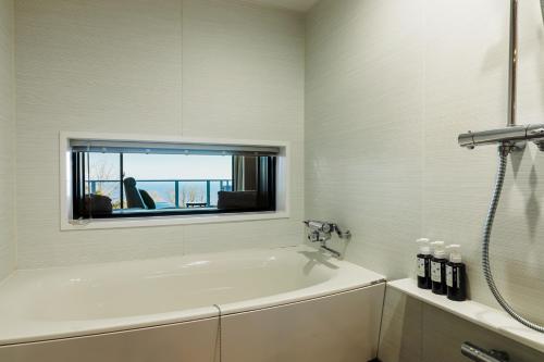 a white bathroom with a tub and a window at the salon 伊豆高原 Hotels & Resort in Ito