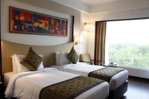 two beds in a hotel room with a window at Gurmon Hotels Sohna Road Gurugram, a member of Radisson Individuals in Sohna