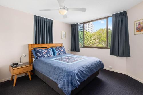 a bedroom with a bed with a blue comforter and a window at Eastbourne U6 80 Esplanade Golden Beach in Caloundra