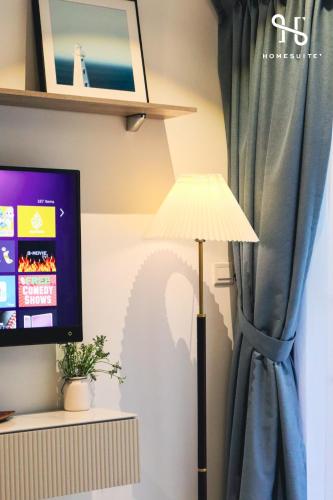 a lamp and a television with a blue curtain at Homesuite' Home at Aeropod SOVO in Kota Kinabalu