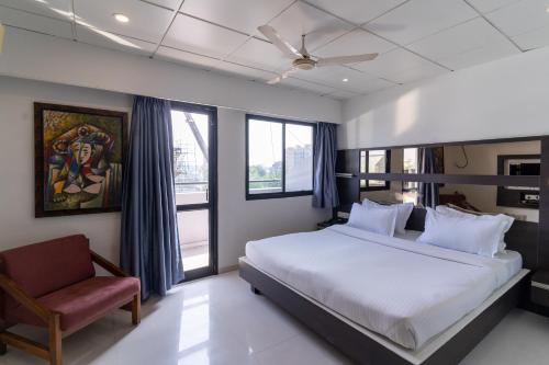 a bedroom with a bed and a chair and windows at Hotel Parkland Manage by G Express in Ahmedabad
