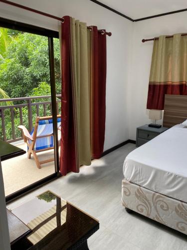 a bedroom with a bed and a balcony with a chair at Mer Riviere Self Catering Apartment in Beau Vallon