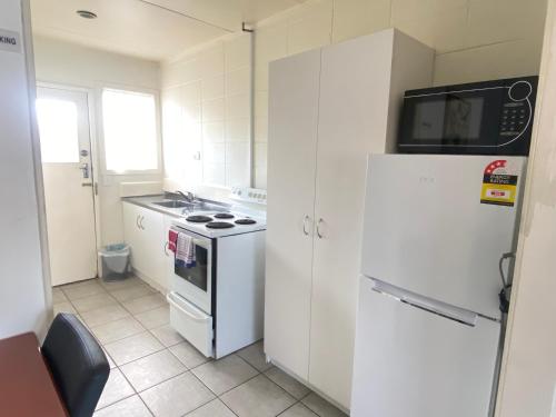 a kitchen with a white refrigerator and a stove at Kowhai Motel Rotorua in Rotorua