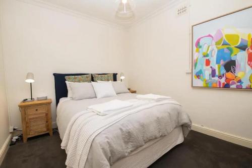 a white bedroom with a bed and a painting on the wall at Orana Cottage in Orange