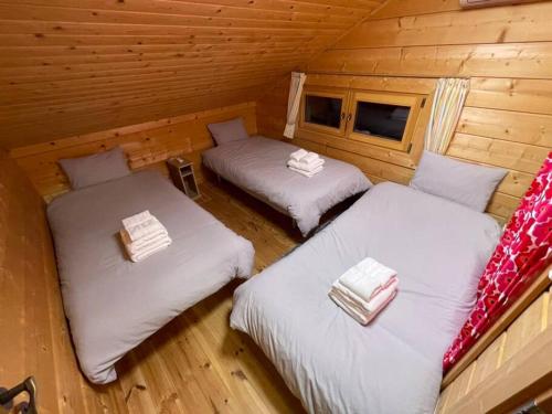 2 camas en una cabaña de madera con sábanas blancas en 浅間山を眺めるフインランドログハウス en Kutsukake
