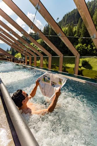 a man in a swimming pool reading a newspaper at ZillergrundRock Luxury Mountain Resort in Mayrhofen