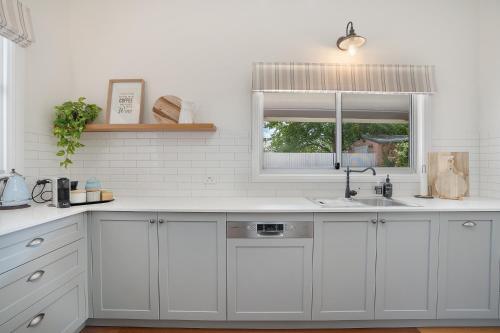 cocina con armarios blancos, fregadero y ventana en ‘Endsleigh Cottage’ - Modern Luxury, Aged Charm, en Cessnock