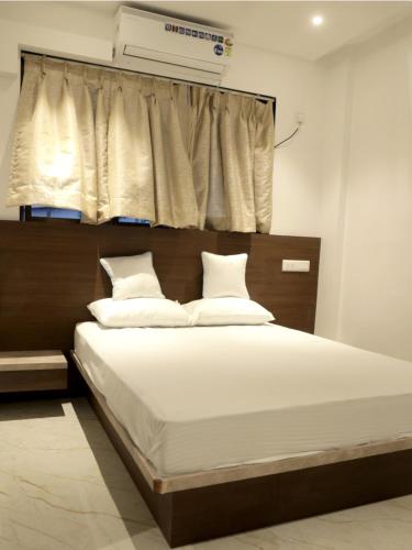 a bedroom with a bed with white sheets and a window at Hotel Majestic in Ulhasnagar