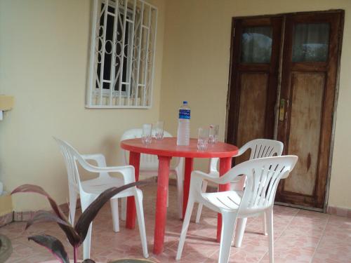 a red table with white chairs and a bottle of water on it at Fayes Apartments in Brusubi