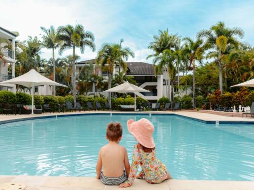 two children sitting next to a swimming pool at Mercure Gold Coast Resort in Gold Coast