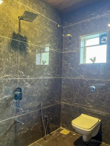 a bathroom with a toilet and a glass shower at Elsewhere Villa by Hill Staytion in Mahabaleshwar