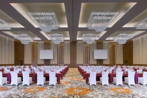 Sheraton Qinhuangdao Beidaihe Hotel في تشنهوانغداو: قاعة اجتماعات وكراسي بيضاء وشاشات بيضاء