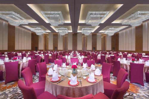 Sheraton Qinhuangdao Beidaihe Hotel في تشنهوانغداو: قاعة احتفالات كبيرة مع طاولات وكراسي أرجوانية