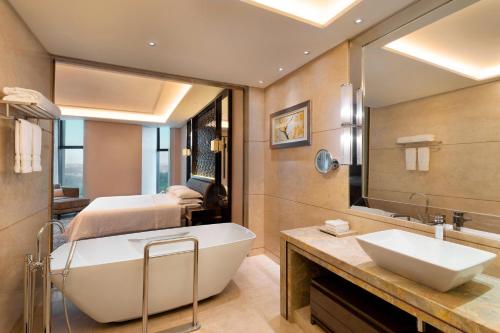 een badkamer met een bad, een wastafel en een bed bij Sheraton Changchun Jingyuetan Hotel in Changchun
