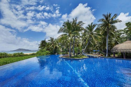 a pool at a resort with palm trees and the ocean at Four Points by Sheraton Shenzhou Peninsula Resort in Wanning