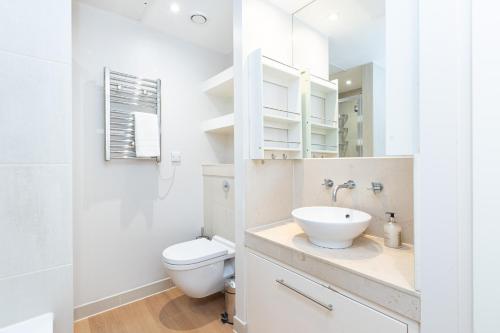a white bathroom with a toilet and a sink at Luxurious Modern 3BR Flat in Prime Canary Wharf in London