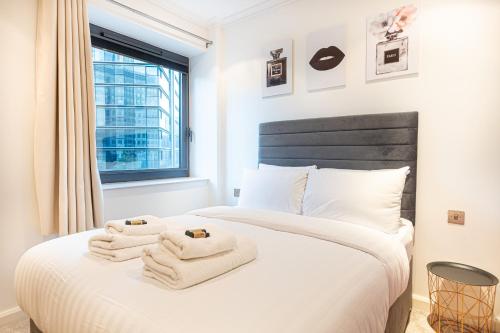 Luxurious Modern 3BR Flat in Prime Canary Wharf في لندن: غرفة نوم بسرير ابيض عليها مناشف