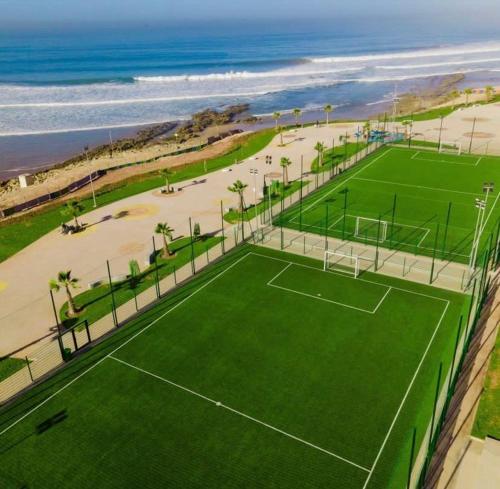 a tennis court next to a beach with the ocean at Résidence Miftah essahil anza agadir in Agadir