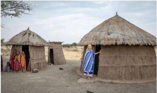 una mujer parada frente a dos chozas en Mombo Maasai Culture Homestay, 